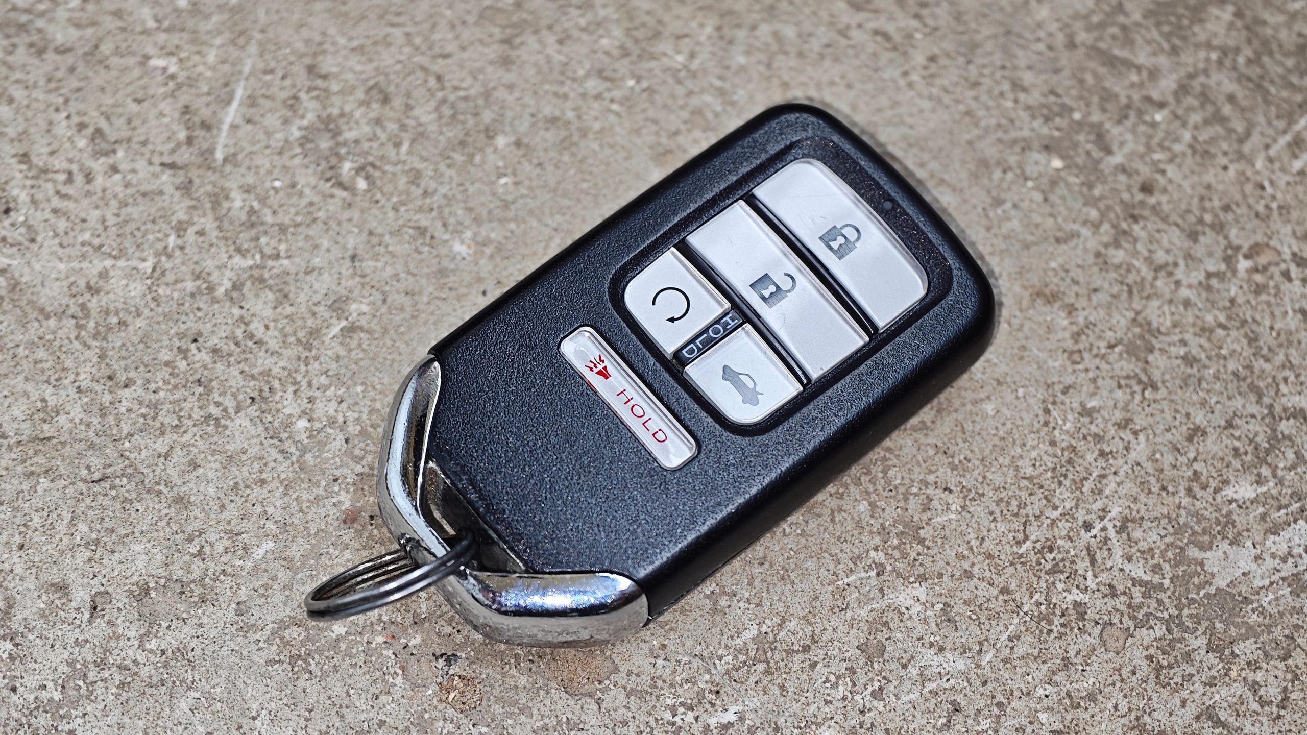 Car key remote featuring multiple buttons for locking, unlocking, and starting vehicles, resting on an industrial background