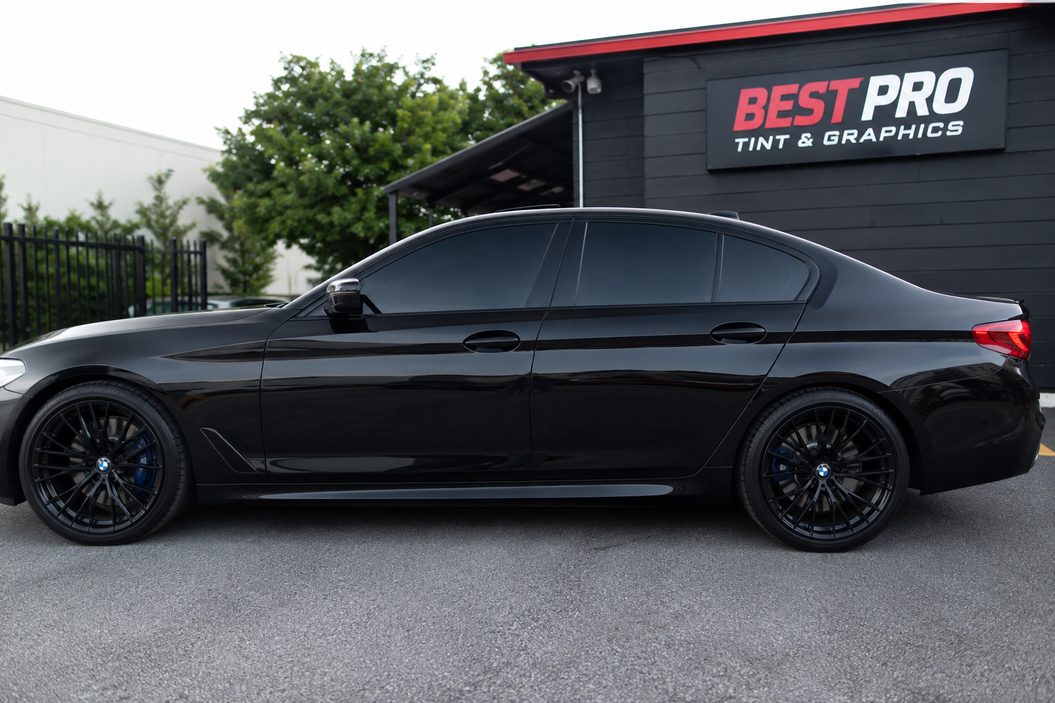 Black BMW sedan with tinted windows parked in front of Best Pro Tint & Graphics shop