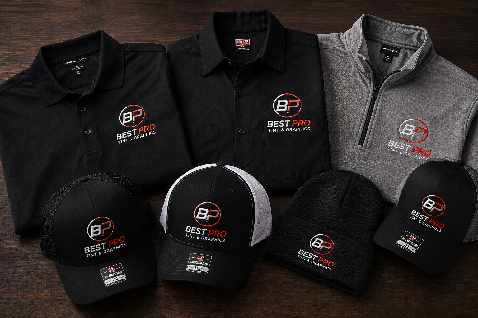 Best Pro Tint & Graphics branded apparel and hats arranged on a wooden surface