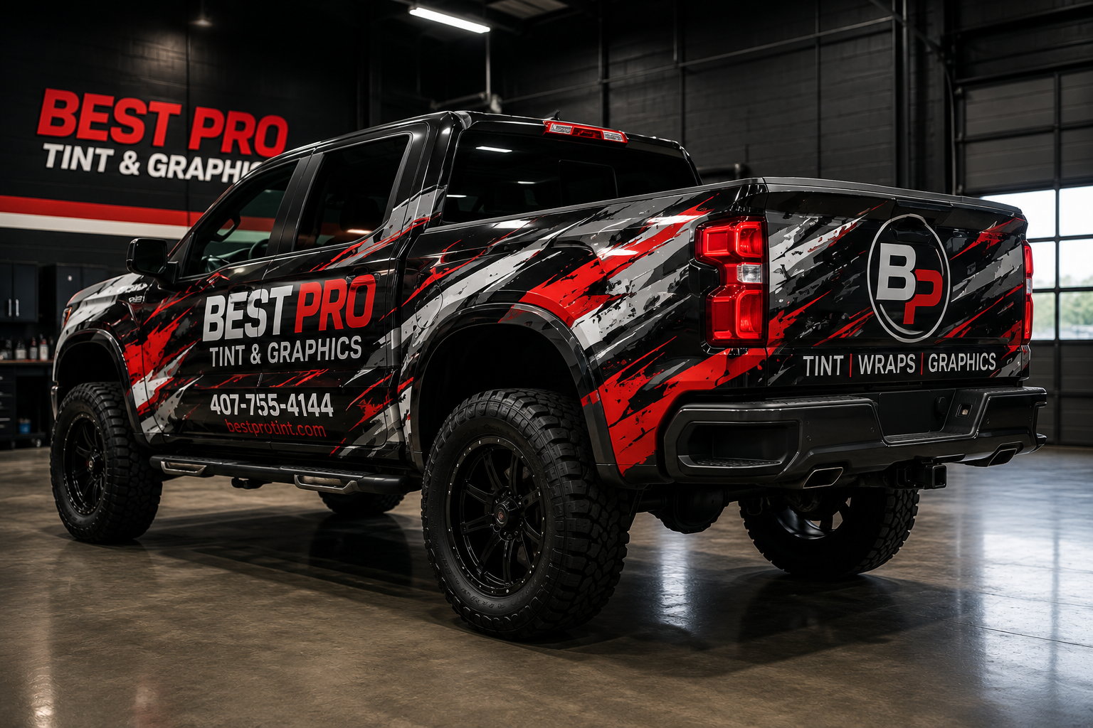 Black pickup truck with red and white Best Pro Tint & Graphics wrap inside a professional shop